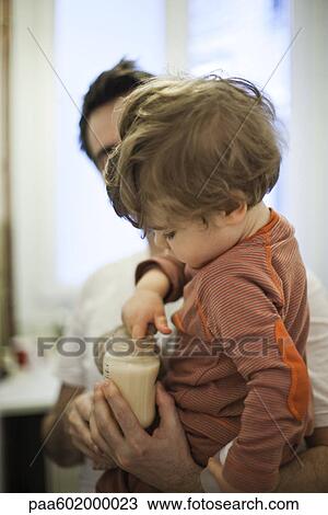 Toddler boy in father's arms, testing temperature of milk in baby bottle View Large Photo Image Stock Image - Toddler boy in father's arms, testing temperature of milk in baby bottle. Fotosearch