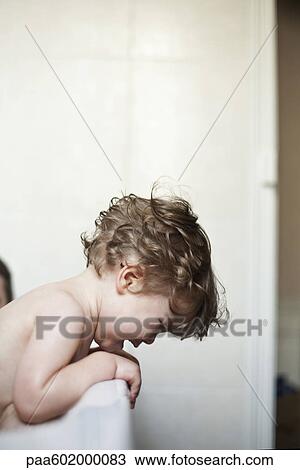 Stock Image - Toddler boy leaning over side of bathtub crying. Fotosearch