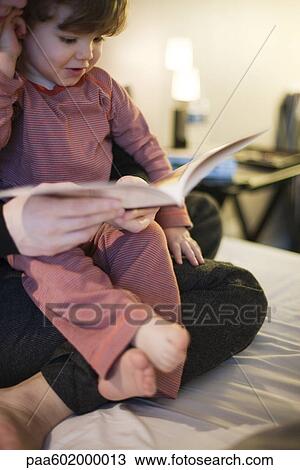 Stock Image - Toddler boy sitting in parent's lap, looking at book, cropped. Fotosearch