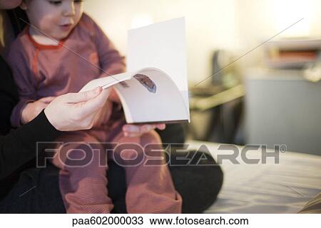 Stock Image - Toddler boy sitting in parent's lap, looking at book, cropped. Fotosearch