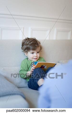 Picture - Toddler boy sitting on couch with book in hands. Fotosearch