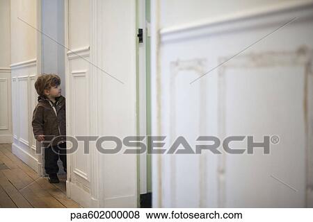 Stock Photo - Toddler boy standing in hall, peeking in doorway. Fotosearch