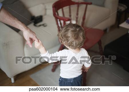 Picture - Toddler holding on to father's hand, walking toward sofa, cropped. Fotosearch