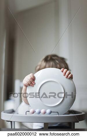 Toddler sitting in high chair, holding plate in front of face View Large Photo Image Stock Image - Toddler sitting in high chair, holding plate in front of face. Fotosearch
