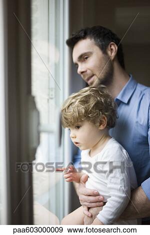 Stock Photo - Father and toddler son looking out window, portrait. Fotosearch