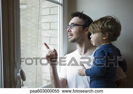 Stock Photography - Father and toddler son looking out window together. Fotosearch