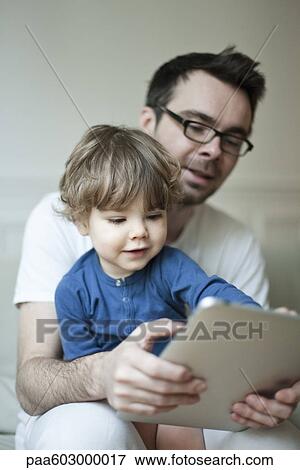 Father and young son looking at digital tablet together View Large Photo Image Stock Photo - Father and young son looking at digital tablet together. Fotosearch