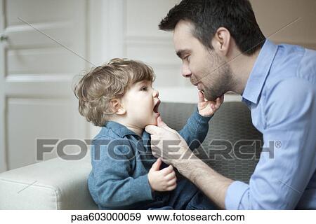 Stock Photo - Father examining toddler son's teeth, portrait. Fotosearch