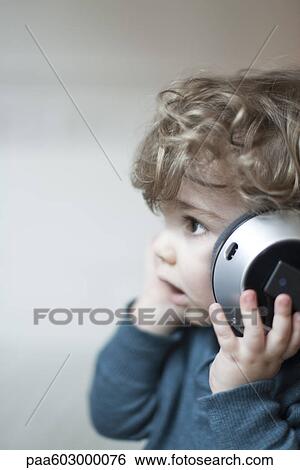 Stock Photograph - Toddler boy listening to music with headphones, portrait. Fotosearch