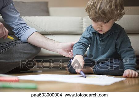 Picture - Toddler boy sitting on floor with father, drawing on paper. Fotosearch