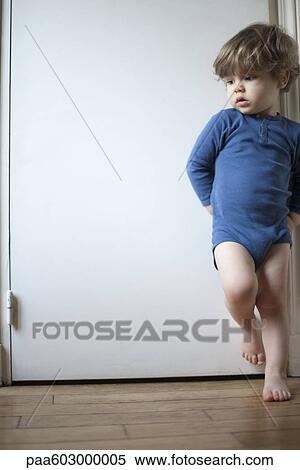 Toddler boy standing on one leg against door, looking away in thought, portrait View Large Photo Image Stock Photography - Toddler boy standing on one leg against door, looking away in thought, portrait. Fotosearch