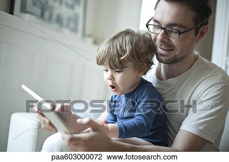 Toddler boy watching father using digital tablet with surprised expression View Large Photo Image Stock Image - Toddler boy watching father using digital tablet with surprised expression. Fotosearch
