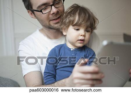 Toddler boy watching father using digital tablet View Large Photo Image Stock Photograph - Toddler boy watching father using digital tablet. Fotosearch
