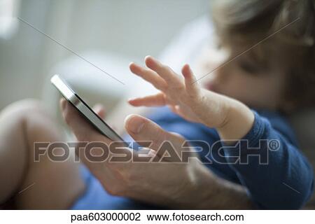 Stock Image - Toddler touching father's cell phone. Fotosearch