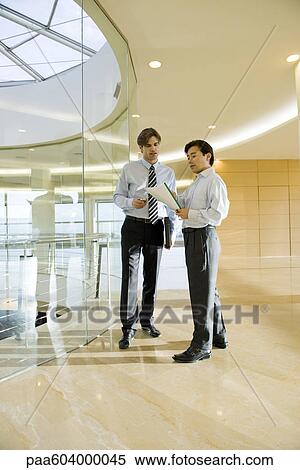 Businessmen discussing document in corridor View Large Photo Image Stock Photography - Businessmen discussing document in corridor. Fotosearch