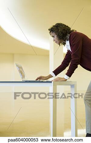 Businesswoman leaning against desk, using laptop computer View Large Photo Image Stock Image - Businesswoman leaning against desk, using laptop computer. Fotosearch
