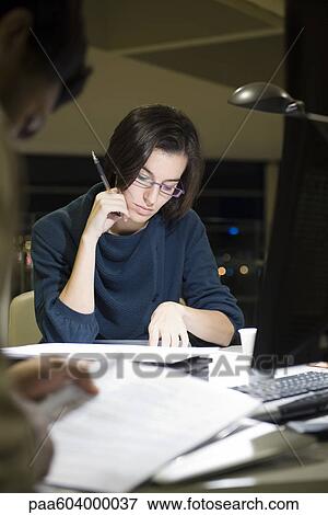Colleagues reading documents in office at night View Large Photo Image Stock Photo - Colleagues reading documents in office at night. Fotosearch