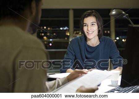 Stock Image - Colleagues working on project together in office at night. Fotosearch