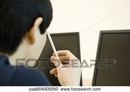 Young man looking at computer monitors, holding pencil against head in thought View Large Photo Image Stock Image - Young man looking at computer monitors, holding pencil against head in thought. Fotosearch