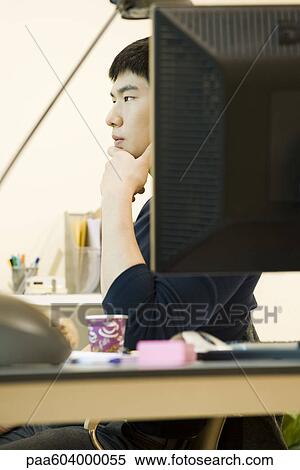 Young man sitting at desk, looking away in thought View Large Photo Image Stock Photography - Young man sitting at desk, looking away in thought. Fotosearch