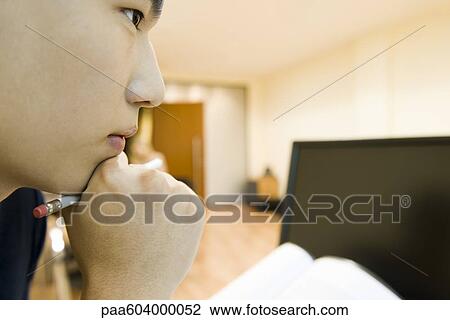 Stock Image - Young man with hand under chin, looking away in thought. Fotosearch