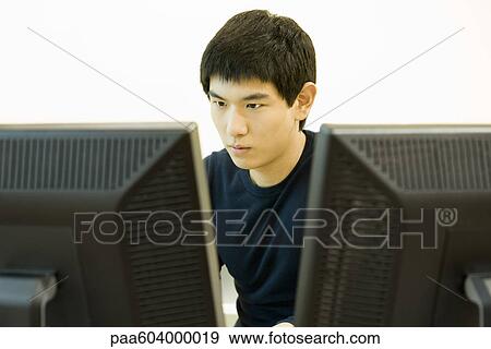 Young man working on computer with two monitors View Large Photo Image Stock Photo - Young man working on computer with two monitors. Fotosearch