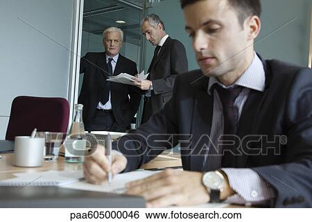 Executives in discussion, young businessman working in foreground View Large Photo Image Stock Photograph - Executives in discussion, young businessman working in foreground. Fotosearch