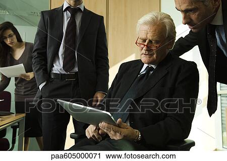 Executives looking down at digital tablet and having discussion View Large Photo Image Stock Image - Executives looking down at digital tablet and having discussion. Fotosearch