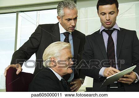 Stock Image - Young businessman showing mature executives how to use digital tablet. Fotosearch