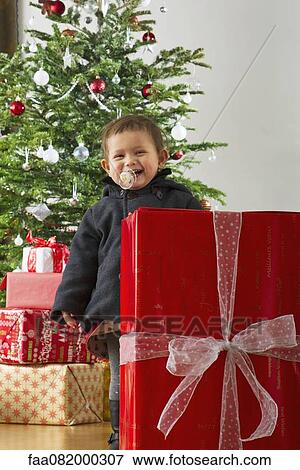 Stock Photo - Baby girl standing behind large Christmas present, laughing. Fotosearch