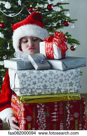 Boy holding stack of Christmas presents with sulky expression on face View Large Photo Image Picture - Boy holding stack of Christmas presents with sulky expression on face. Fotosearch