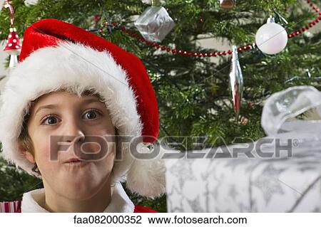Stock Image - Boy in Santa hat making surprised face, portrait. Fotosearch