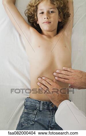Boy lying on examination table, doctor feeling abdomen View Large Photo Image Picture - Boy lying on examination table, doctor feeling abdomen. Fotosearch