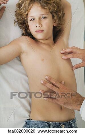 Boy lying on examination table, doctor feeling chest View Large Photo Image Stock Image - Boy lying on examination table, doctor feeling chest. Fotosearch