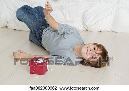 Stock Image - Boy lying on floor beside gift box. Fotosearch