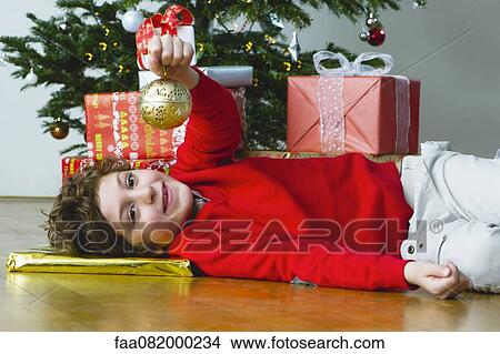 Boy lying on floor by Christmas tree, holding up ornament View Large Photo Image Picture - Boy lying on floor by Christmas tree, holding up ornament. Fotosearch