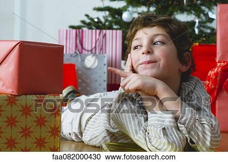 Stock Image - Boy lying on floor pointing at Christmas presents. Fotosearch
