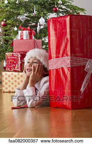Stock Photo - Boy lying on floor with Christmas presents, daydreaming. Fotosearch
