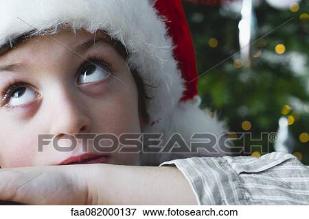 Stock Photo - Boy wearing Santa hat, looking up impatiently. Fotosearch