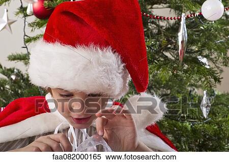 Boy wearing Santa hat, opening Christmas present View Large Photo Image Stock Photography - Boy wearing Santa hat, opening Christmas present. Fotosearch