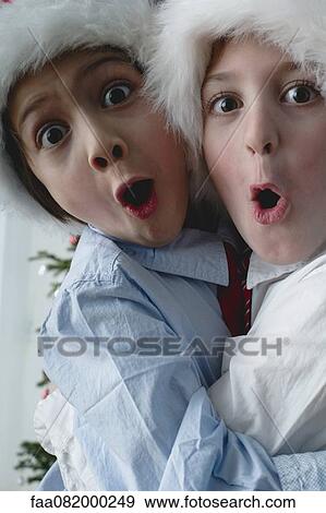 Stock Photo - Boys wearing Santa hats, hugging and making surprised faces. Fotosearch