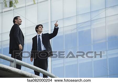 Business associates standing together outdoors, one pointing View Large Photo Image Picture - Business associates standing together outdoors, one pointing. Fotosearch