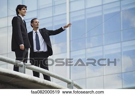 Stock Photo - Business associates standing together outdoors, one pointing. Fotosearch