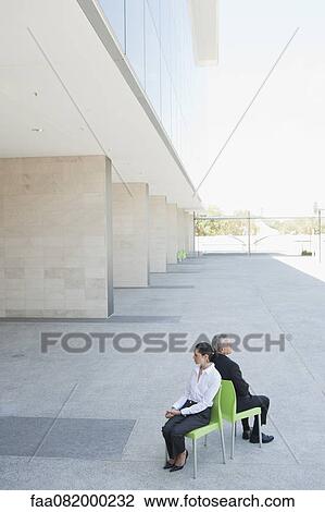 Businessman and businesswoman sitting back to back in chairs outside office building View Large Photo Image Stock Image - Businessman and businesswoman sitting back to back in chairs outside office building. Fotosearch