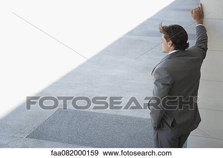 Businessman leaning against wall, looking away in thought View Large Photo Image Stock Photo - Businessman leaning against wall, looking away in thought. Fotosearch