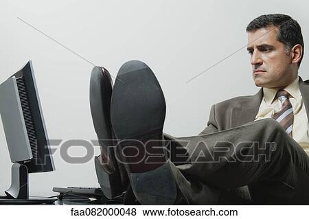 Businessman sitting in office with feet up on desk View Large Photo Image Stock Photo - Businessman sitting in office with feet up on desk. Fotosearch