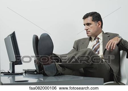Businessman sitting in office with feet up on desk View Large Photo Image Stock Photograph - Businessman sitting in office with feet up on desk. Fotosearch