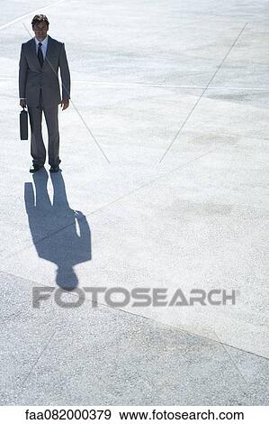 Stock Photo - Businessman standing outdoors with briefcase in hand. Fotosearch