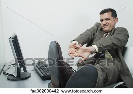 Businessman stretching at desk in office View Large Photo Image Stock Image - Businessman stretching at desk in office. Fotosearch
