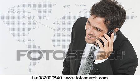Stock Image - Businessman talking on cell phone, world map in background. Fotosearch
